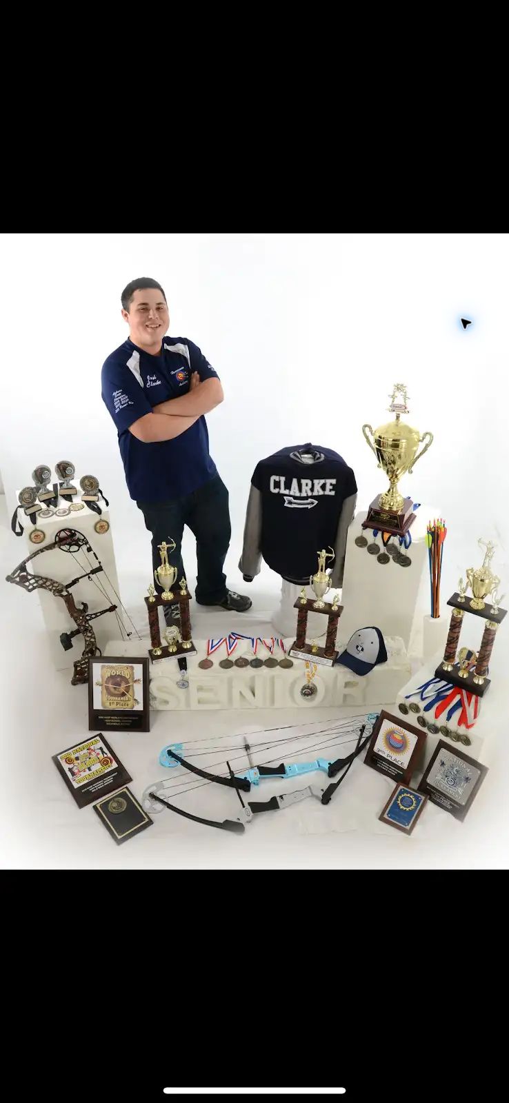 Coach Joshua Clarke with trophies medals bows and plaques from his competitive archery career